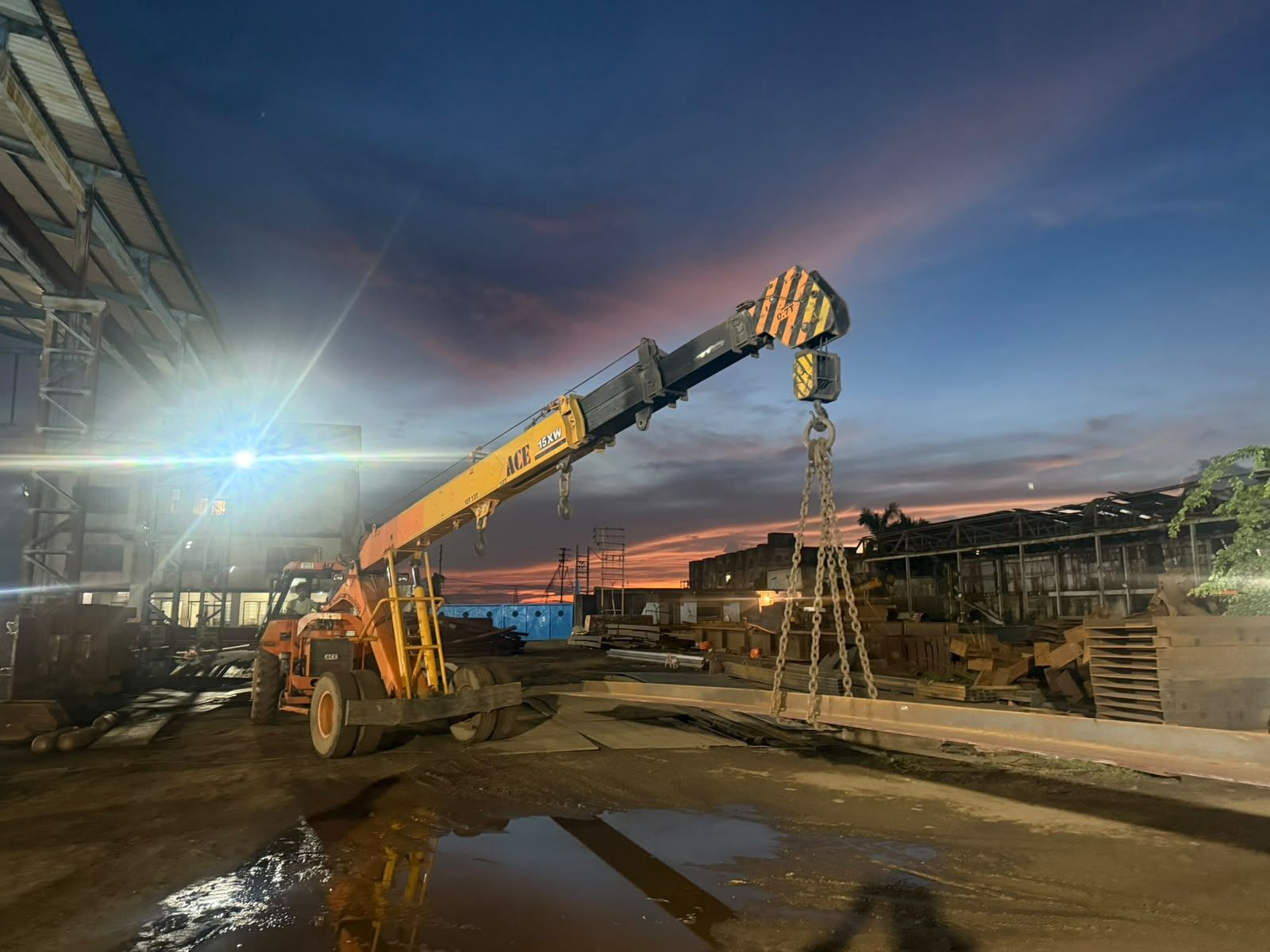 Mobile crane and steelwork in the lit fabrication yard at dusk