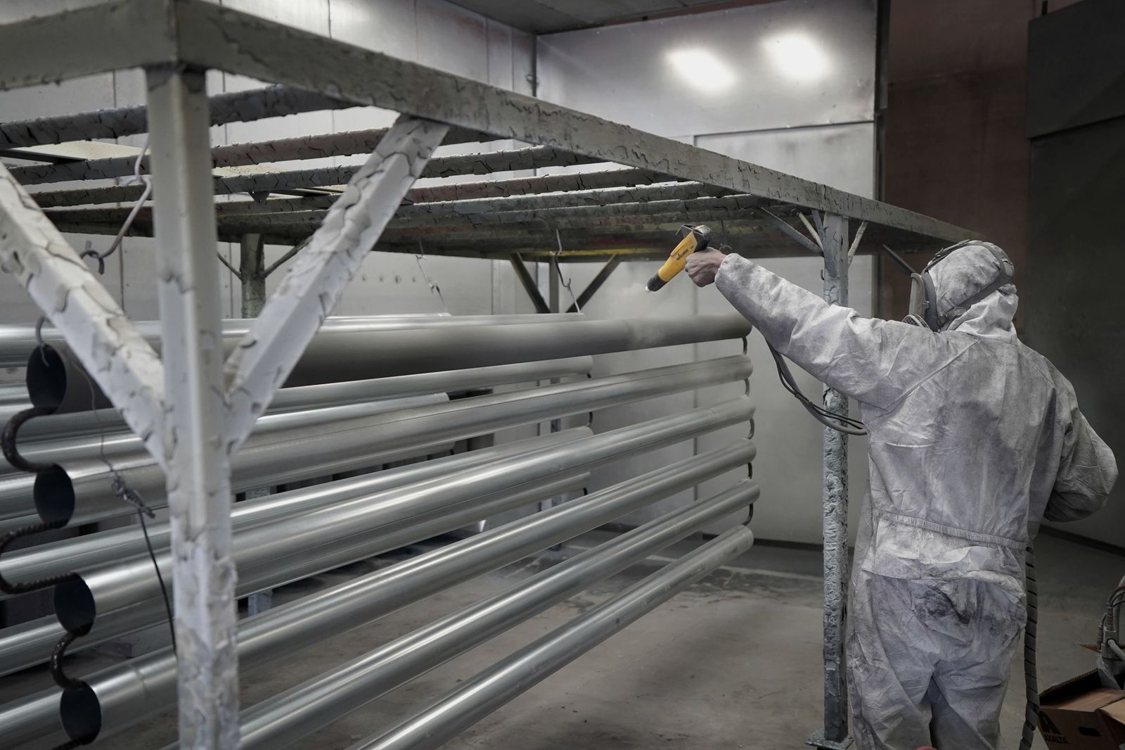 Painter in protective gear spraying steel members in a paint booth